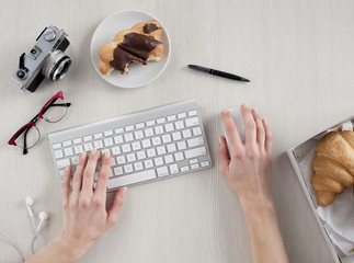 Top view of woman hands typing on keyboard with office supplies around
