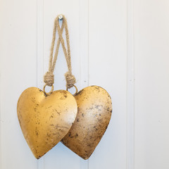 Two golden hearts on white wooden background
