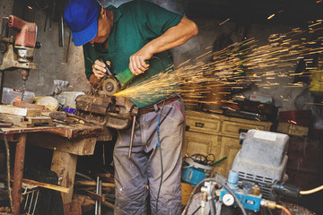 Craftsman sawing metal with disk grinder in workshop.