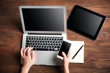 Poster - Modern tablet, mobile phone, and female hands using laptop, on the wooden background