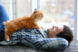 Fototapeta Koty - Young man with fluffy cat lying on a carpet