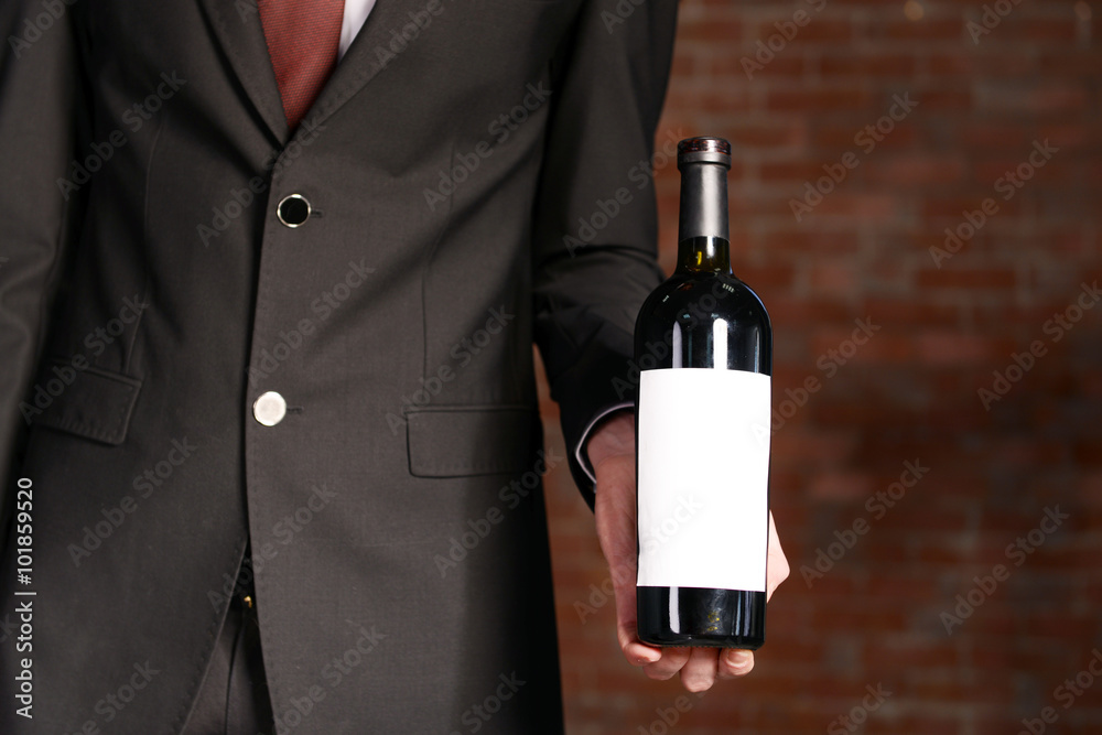 Man holding a bottle of red wine in hands on brick wall background