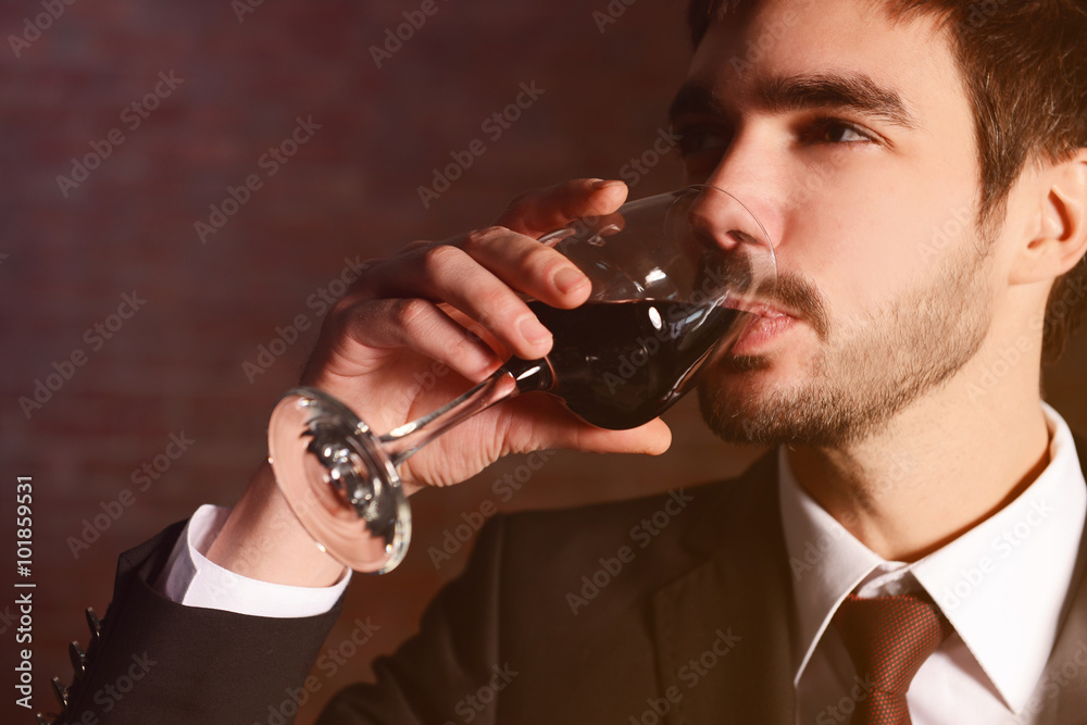Man testing red wine in glass on brick wall background
