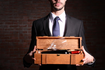 Wall Mural - Man holding a bottle of red wine and glass in wooden box on brick wall background