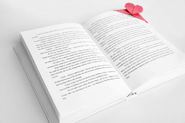 Book and heart shaped bookmark on a light wooden background