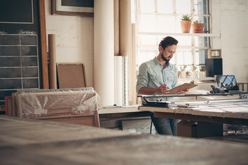 Entrepreneur in his workshop checking figures on a clipboard