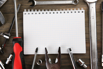 Wall Mural - Different kinds of tools with a notebook on wooden background, closeup