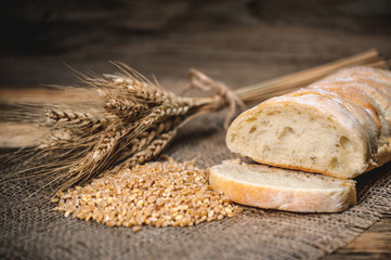 a ciabatta bread with wheat on stackcloth on a wooden rustic background