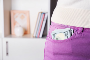 Dollars in pocket of violet pants on unfocused background closeup