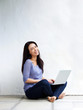 © mimagephotos - Happy young woman sitting on floor at home with a laptop