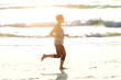 © mimagephotos - Active young woman running on beach with bright sunlight