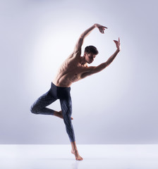 Wall Mural - Athletic ballet dancer in a perfect shape performing over the grey background.