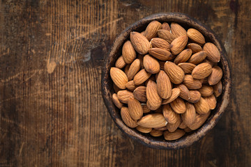 Wall Mural - Almonds in brown bowl on textured wooden background, top view. Copy space on left side