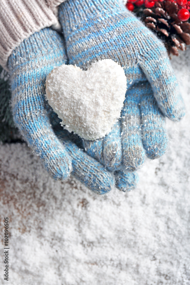 Female hands in blue mittens with decorative heart on snow background