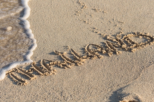 Inscription Thailand on sandy beach with wave's foam