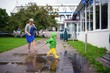 Happy little boy in not getting wet clothes plays in pool on street with grandmother