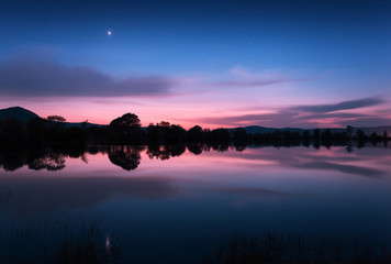Wall Mural - mountain lake with stars and reflected clouds in water. night