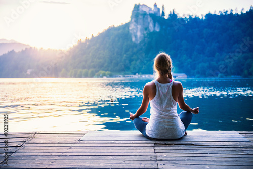 Yoga lotus. Young woman doing yoga by the lake, sitting in lotus.