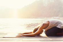 Sun Salutation Yoga. Young Woman Doing Yoga By The Lake, Bathing In Sunlight.