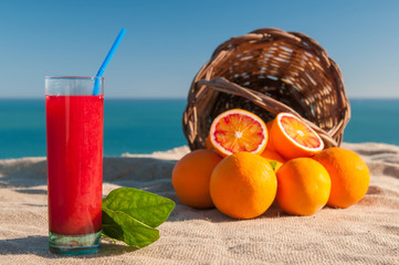 Fresh orange juice and a full wicker basket on a piece of juta with blue sea in the background