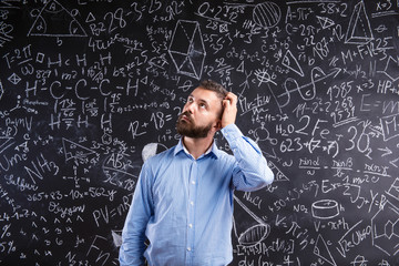 Teacher scratching his head against big blackboard with mathemat