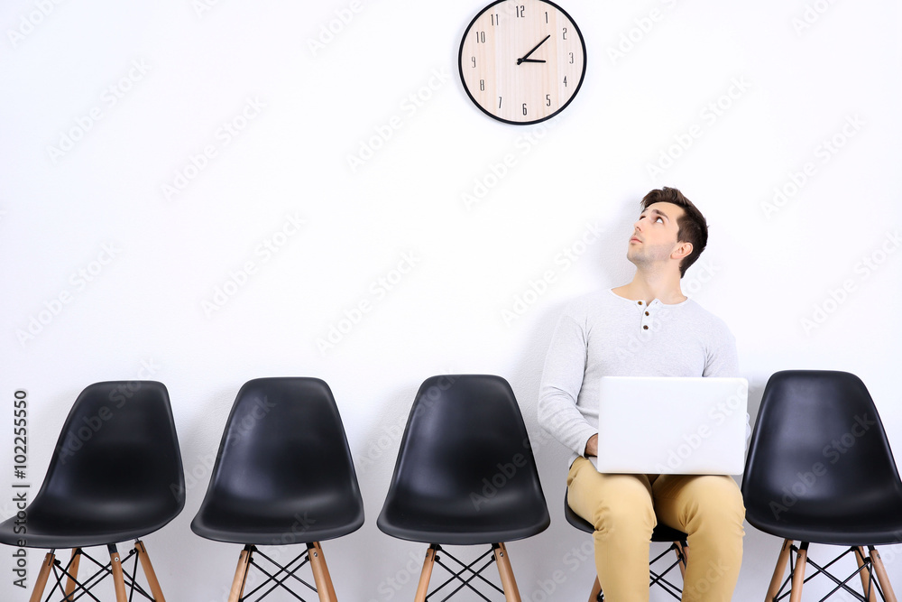 Young man sitting on a chair and looking at the clock in white hall