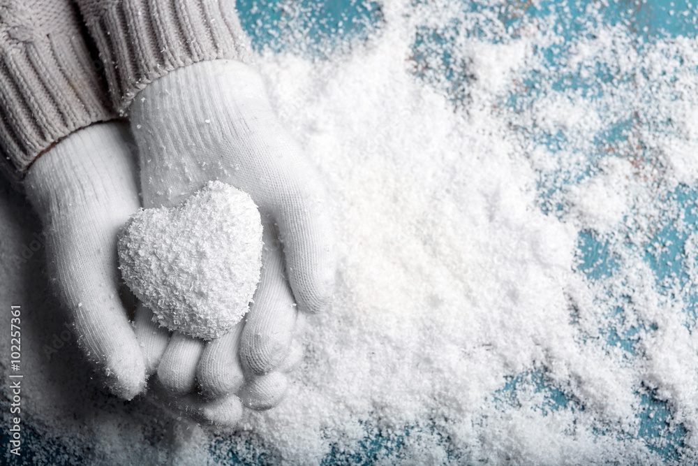 Female hands in mittens with heart on snow background