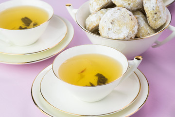 Two cups with green tea and cookies.