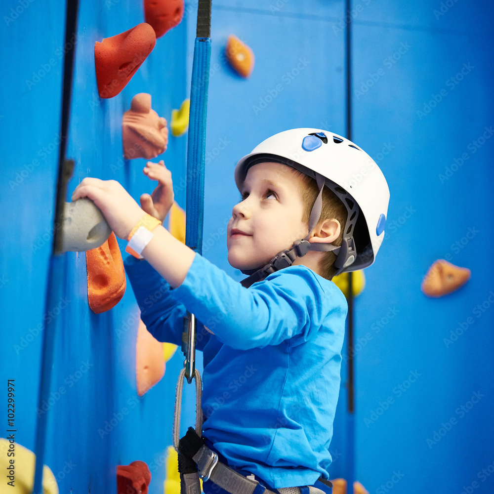 Little boy is climbing in sport park on blue wall - obrazy, fototapety, plakaty 