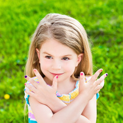 Wall Mural - Beautiful smiling blond little girl with long hair and many-colored manicure, outdoor portrait on green grass background