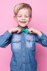 Wall Mural - Young handsome kid smiling with blue shirt and butterfly tie. Studio portrait over pink background