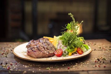 Delicious dinner with beef steak, potatoes and salad on a wooden table, near the fireplace