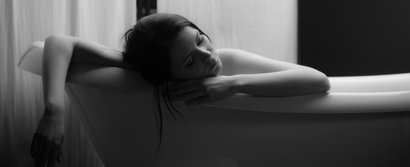 Black and white portrait of a beautiful relaxed brunette woman sleeping in the bath and dreaming