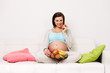 Pregnant happy smiling woman sitting on a sofa eating healthy food snack. Young beautiful mom expecting Baby. Pregnant Woman Belly. Maternity concept. Baby Shower
