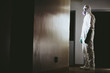 © Mint Images - Man wearing a hazardous material protective clean suit, facing bright light in hallway