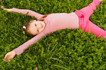 Portrait of a cute little girl of 7 years old in the park, laying on grass, wearing red clothes