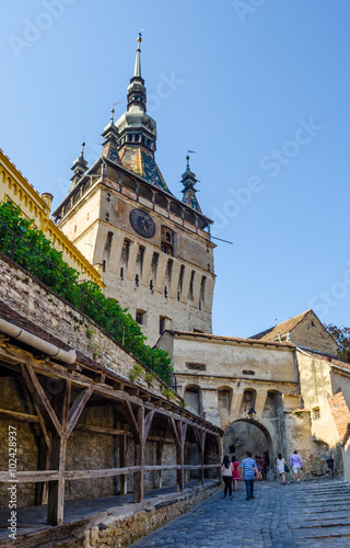 Fotografie, Obraz Clock tower sided by old building inside medieval town of Sighisoara, Transylvan