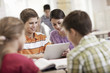 © Mint Images - A group of students seated at a desk in a lesson talking to each other and sharing a digital tablet.