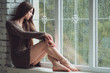 © sergiophoto - Beautiful young woman sitting alone near window with rain drops. Sexy and sad girl. Concept of loneliness