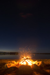 sparking camp fire beside lake under a starry sky