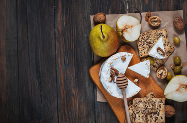 Camembert cheese with walnuts, honey and pears on rustic table. Glass of white wine