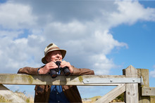 Senior Man With Binoculars Leaning Against Wooden Gate