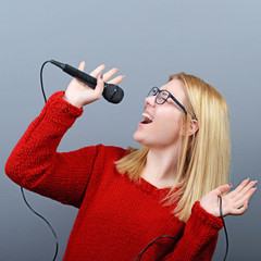 Beautiful woman singing with the microphone against gray backgro