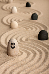 Wall Mural - Stone smiley sticking out of the sand, between white and black stones