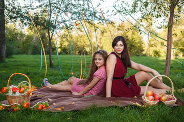 Mom and daughter in the park sitting back to back on a plaid