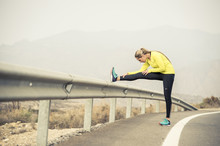 Sport Woman Stretching Leg Muscle After Running Workout On Asphalt Road With Dry Desert Landscape In Hard Fitness Training Session