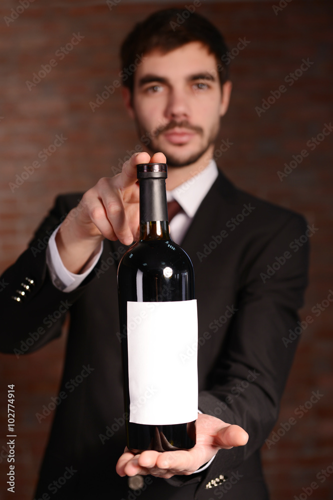 Man holding a bottle of red wine in hands on brick wall background