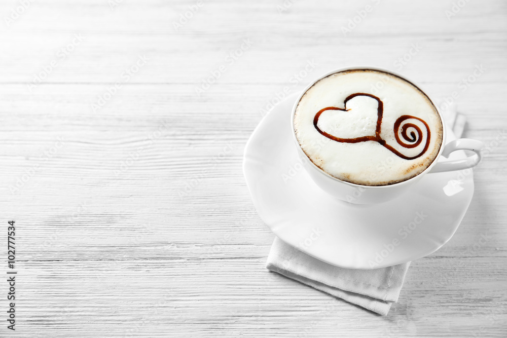 Cup of cappuccino with chocolate syrup on light wooden table