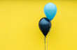 A light blue balloon and a dark blue balloon against a bright yellow wall.