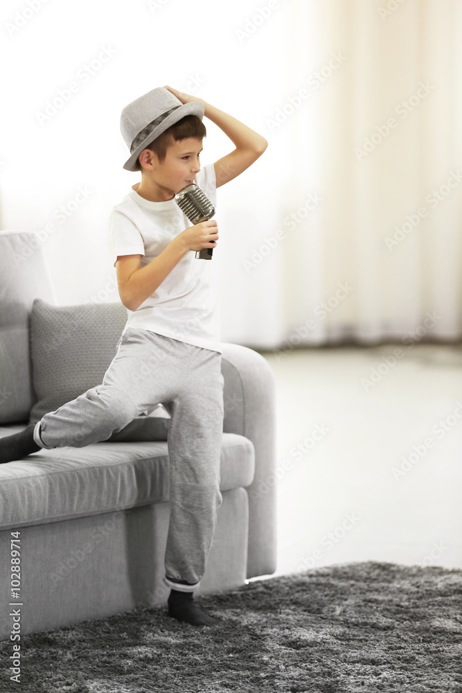 Little boy in a hat singing into the microphone at home